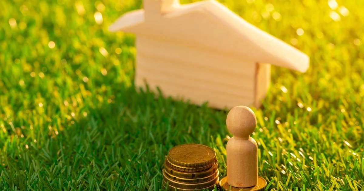 Houten speelgoedhuisje met munten en poppetje op gras — subsidies warmtepomp